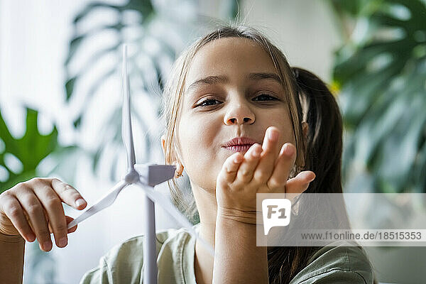 Girl blowing kiss by wind turbine model at home
