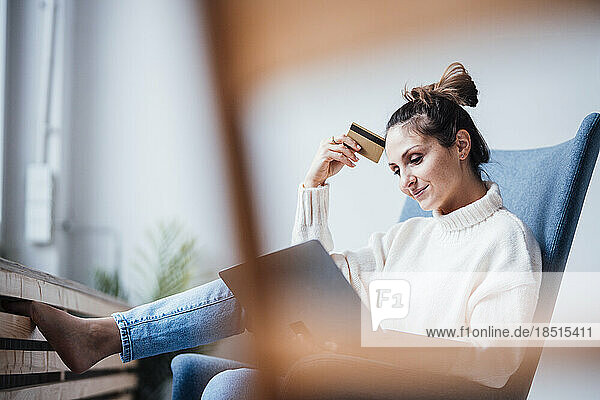 Smiling freelancer with credit card using laptop at home office