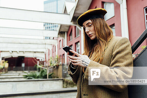 Redhead woman text messaging using mobile phone in front of buildings