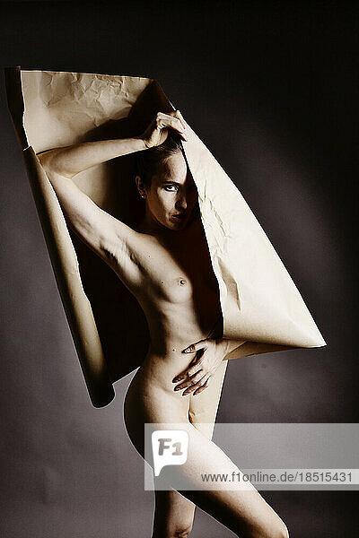 Naked woman with brown paper standing against studio background