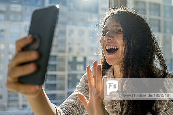 Happy woman talking on video call through smart phone at home