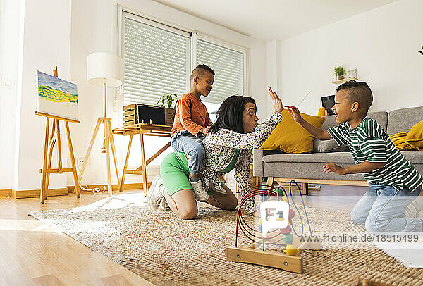Young woman playing with twin sons in living room at home