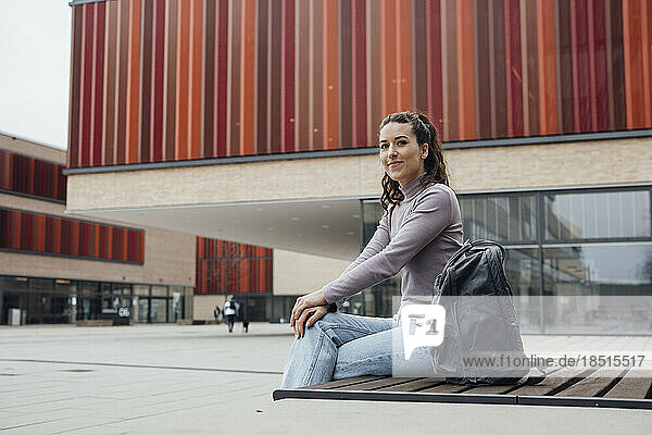Smiling woman with backpack sitting outside building