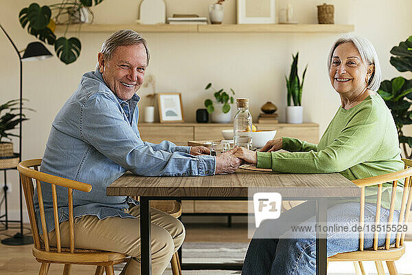 Happy couple holding hands at table in home