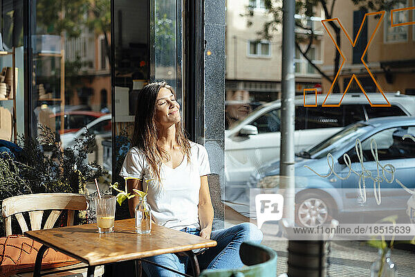 Smiling woman with eyes closed sitting by window in cafe