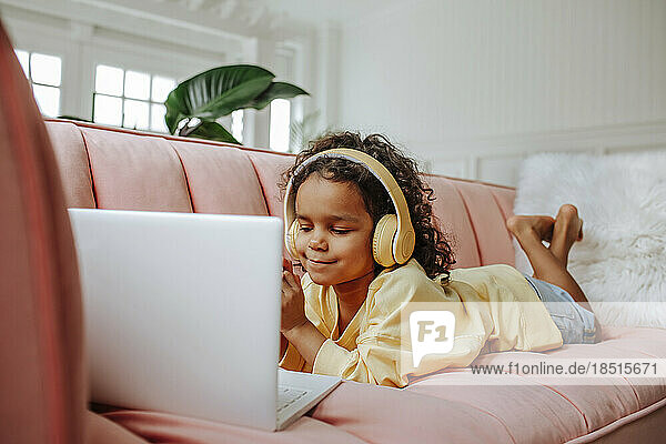 Girl wearing wireless headphones studying on laptop at home