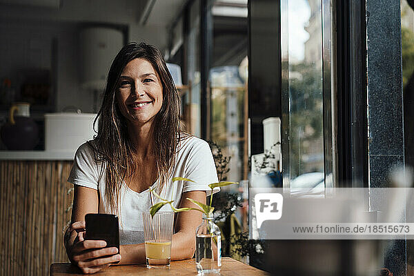 Happy woman sitting with smart phone in cafe