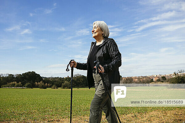 Smiling senior woman walking with hiking poles on hiking path