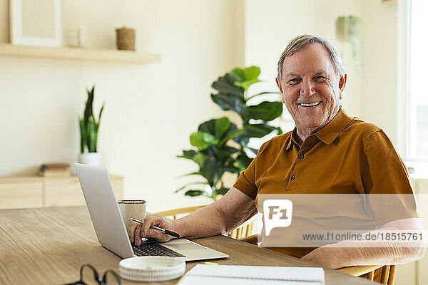 Happy senior man sitting with laptop on table at home