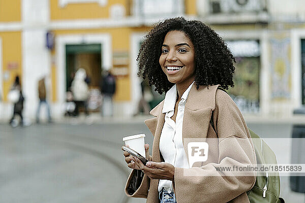 Glückliche junge Frau steht mit Kaffeetasse und Mobiltelefon
