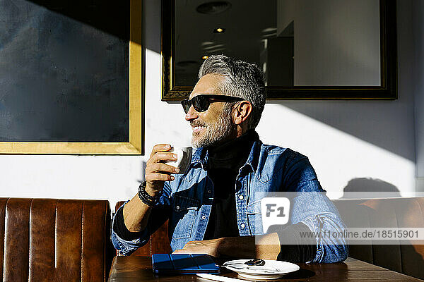 Smiling mature businessman with coffee cup sitting in cafe