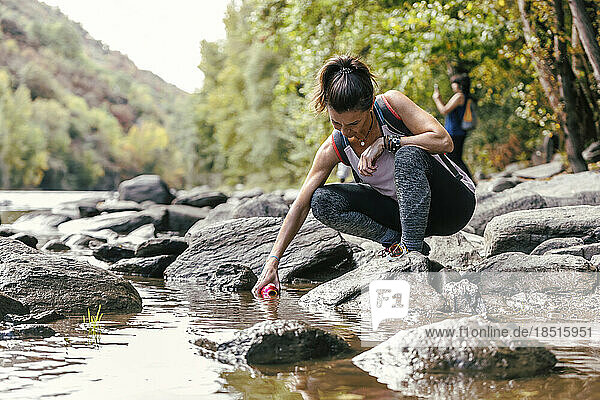 Mother crouching on rock filling water bottle from river
