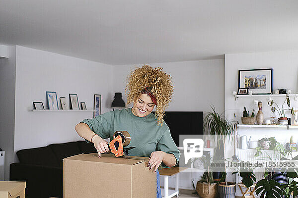 Smiling woman packing box with adhesive tape
