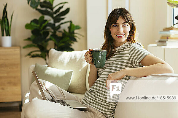 Thoughtful woman with coffee cup sitting on sofa