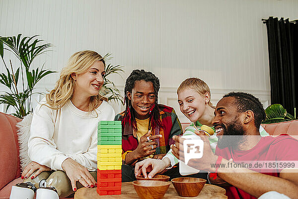 Young man with friends playing toy block game looking at smart phone in living room
