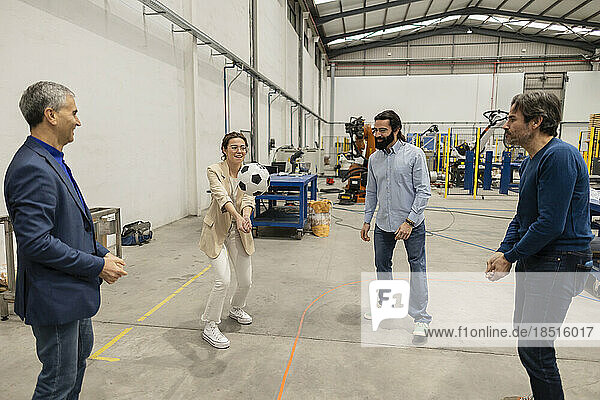 Happy engineers playing volleyball with soccer ball in industry