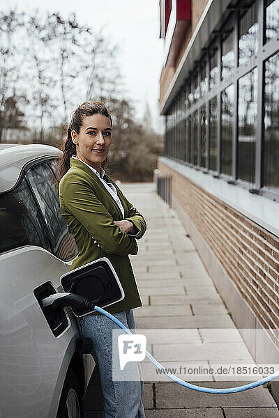 Lächelnde Frau lehnt an Elektroauto mit Ladekabel
