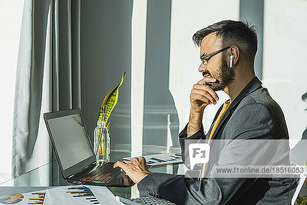 Businessman with hand on chin working on laptop at home office