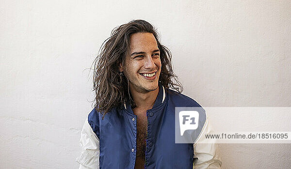 Glücklicher junger Mann mit langen Haaren vor weißer Wand