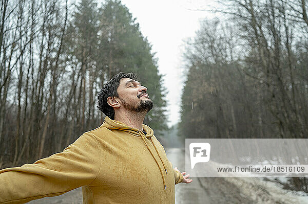 Smiling man with arms outstretched enjoying nature in rainy day