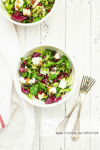Two bowls of mixed vegetarian salad with pomegranate seeds and feta cheese