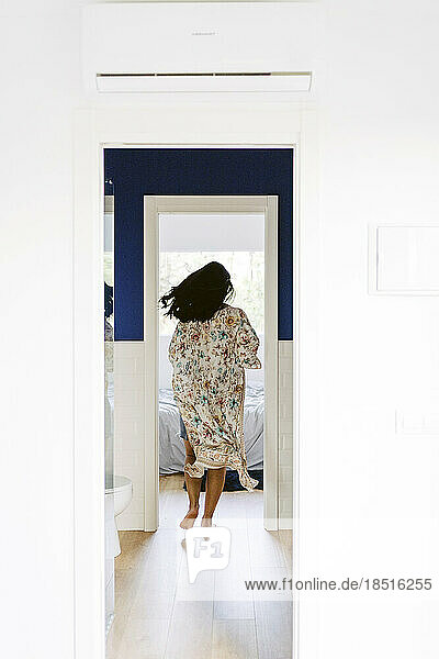Young woman running towards bedroom seen through doorway