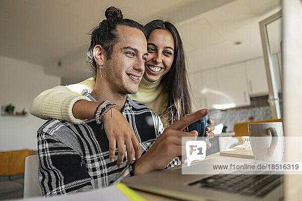 Happy young man discussing with girlfriend over laptop at home office