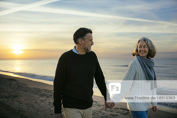 Happy mature woman holding hands and walking at beach