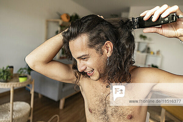 Happy man cutting hair with electric razor at home