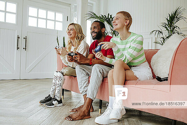Happy young man playing video game with women sitting on sofa at home