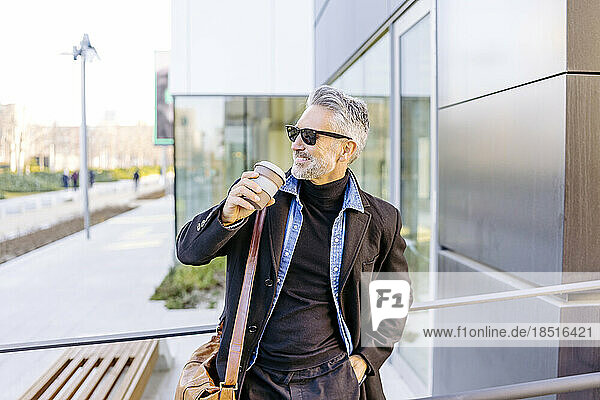 Happy businessman leaning with coffee cup on railing