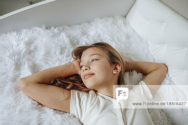 Girl with hands behind head relaxing on fur bed at home