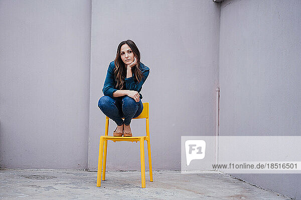 Thoughtful young woman sitting on chair in front of wall