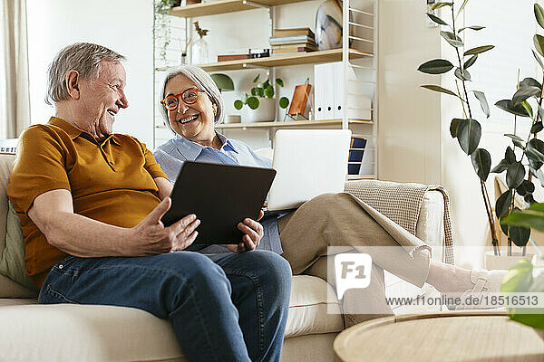 Happy senior couple sitting with tablet computer on sofa in living room