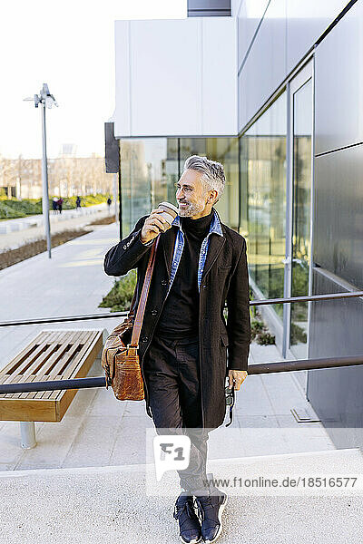Happy mature businessman leaning with coffee cup on railing