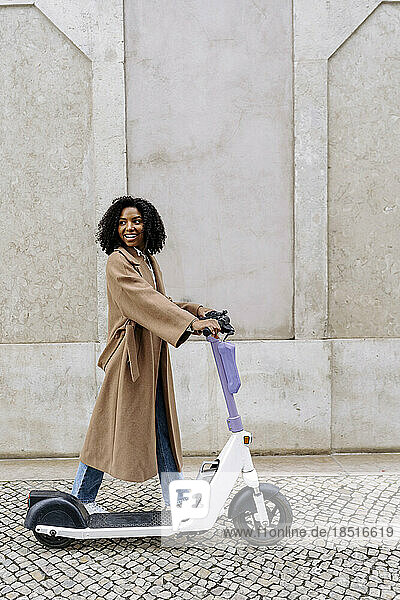Smiling young woman walking with electric push scooter