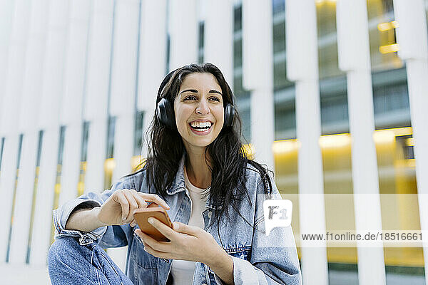 Happy young woman with smart phone in front of building