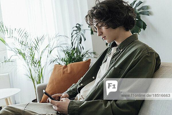 Boy with long hair using smart phone at home
