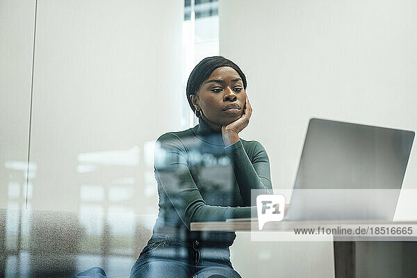 Geschäftsfrau stützt sich auf den Ellenbogen und schaut durchs Fenster auf ihren Laptop