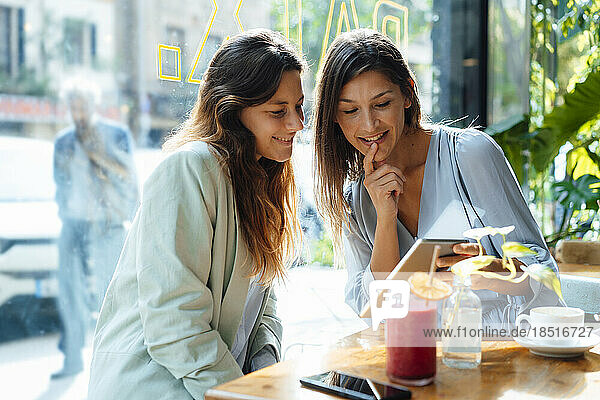 Smiling women sharing tablet PC in cafe