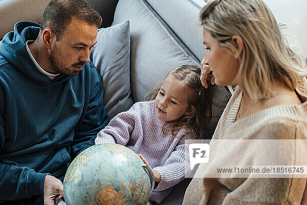 Tochter und Eltern schauen zu Hause auf dem Sofa auf den Globus