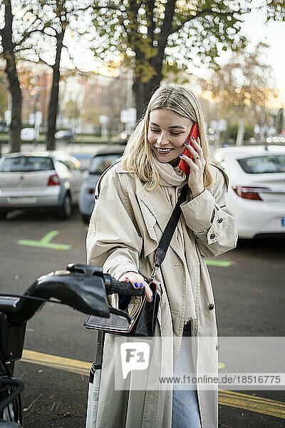 Smiling woman talking on smart phone standing at bicycle parking station