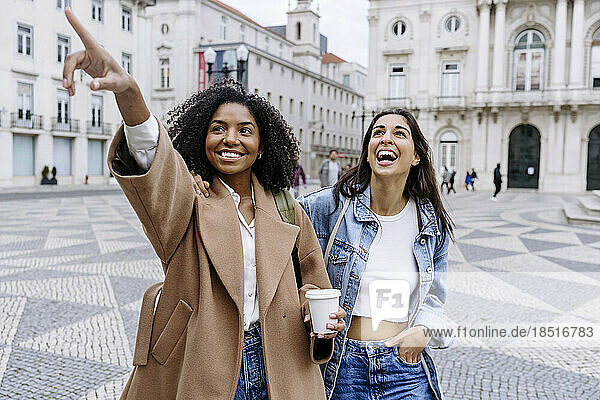 Lächelnde junge Frau gestikuliert und steht mit einer Freundin auf dem Stadtplatz