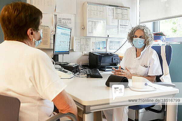 Doctor discussing with senior patient sitting at desk in clinic