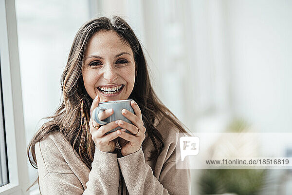 Glückliche junge Frau hält Kaffeetasse zu Hause