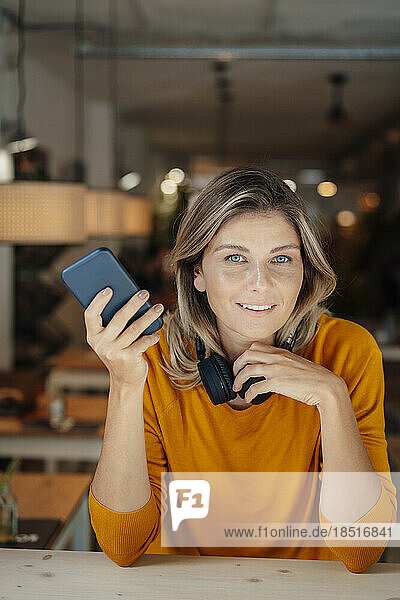 Smiling woman with blond hair holding smart phone in cafe
