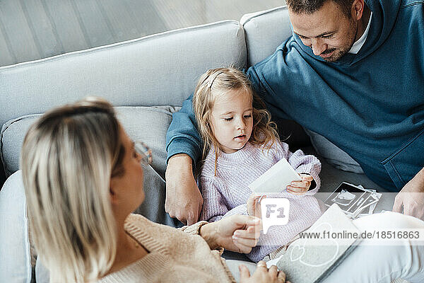 Daughter holding ultrasound image by parents sitting on sofa in living room