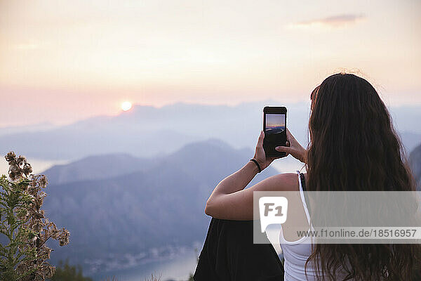 Young woman photographing sunset through smart phone