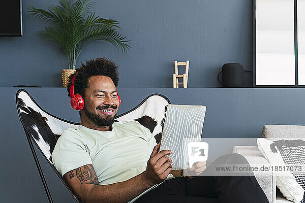 Lächelnder Mann beobachtet Tablet-PC und entspannt sich zu Hause auf einem Stuhl