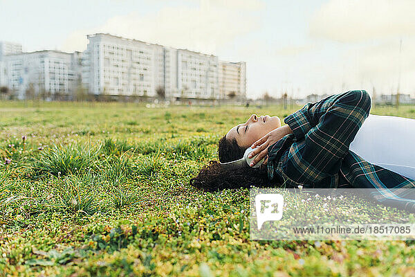 Woman with eyes closed relaxing and listening to music in grass at sunset